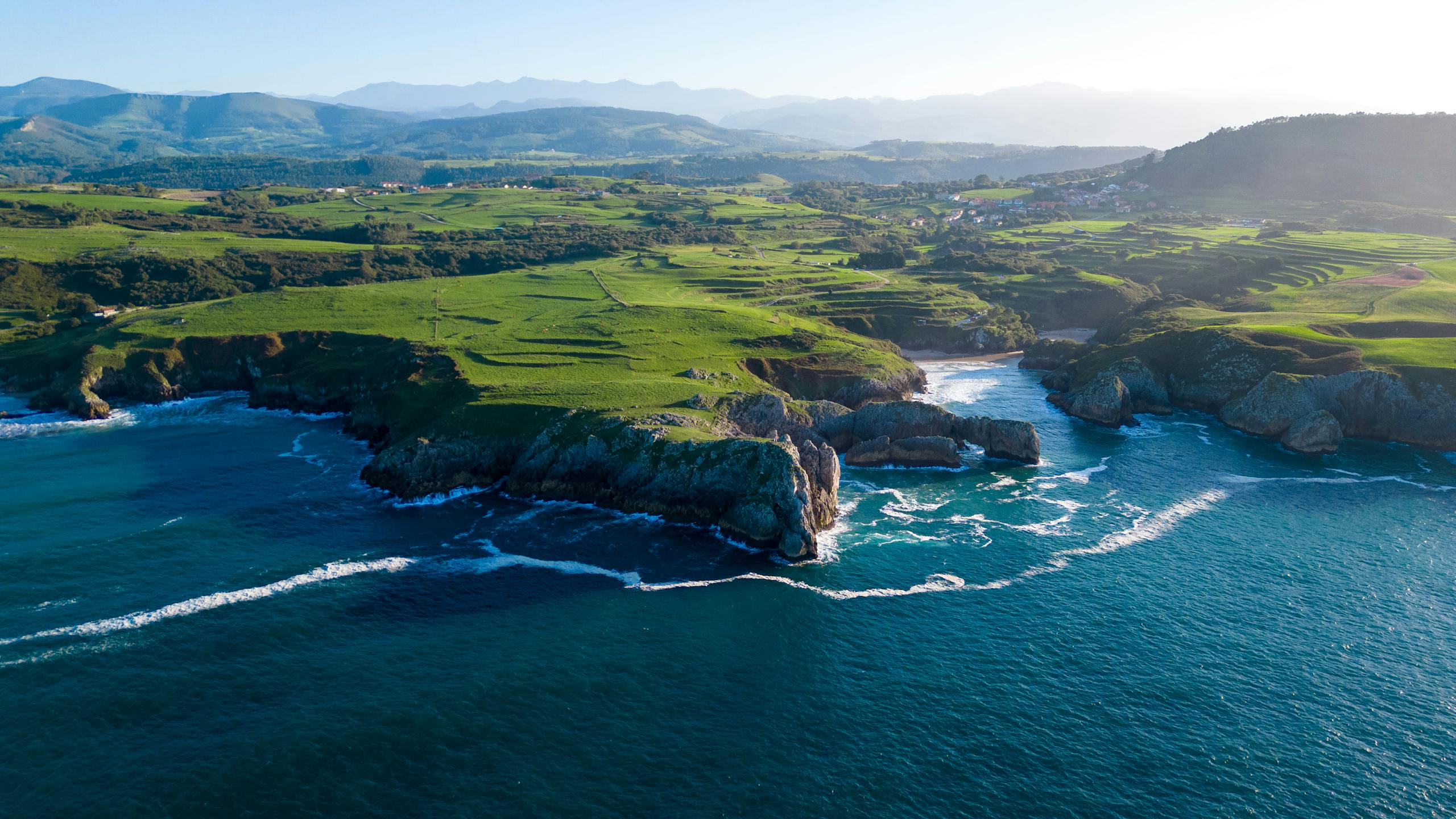 Breathtaking aerial view of Asturias coastline with lush greenery and blue ocean waves.