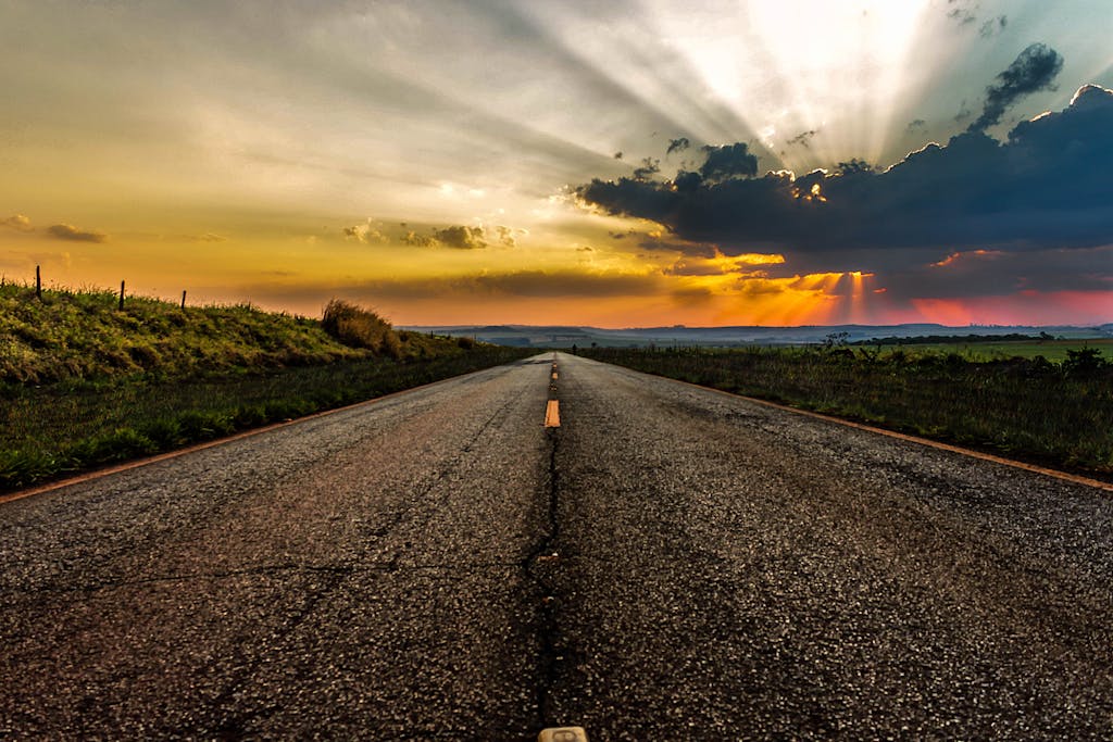 Dramatic sunset over an empty rural highway with vibrant skies and sunrays.