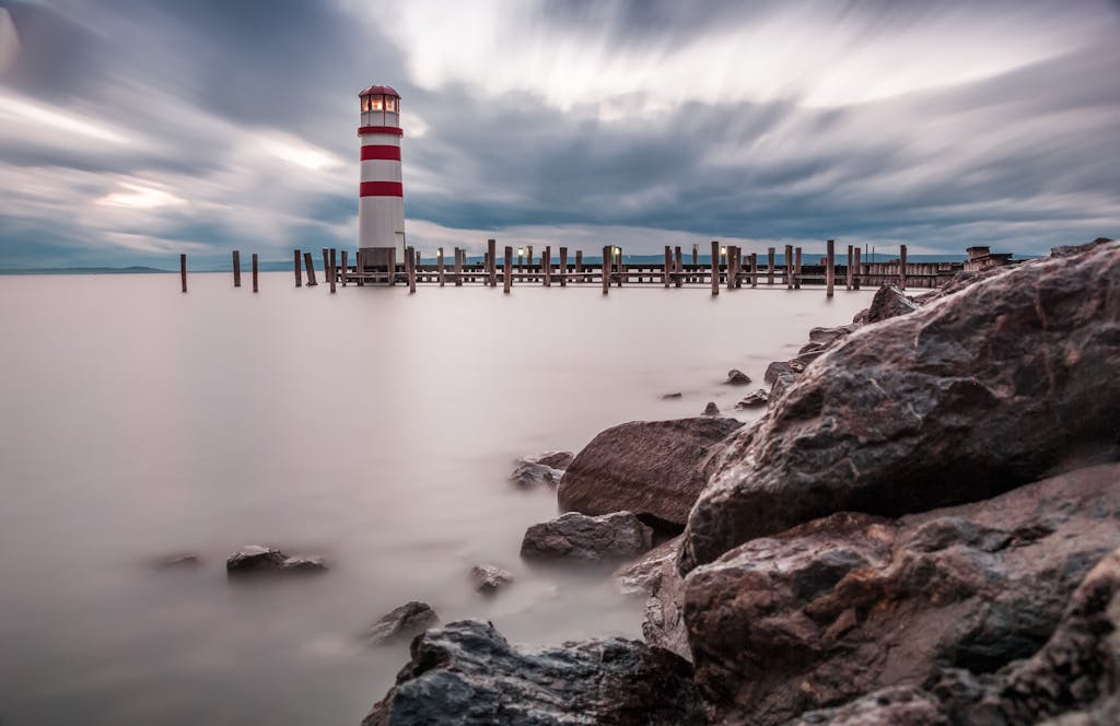 Long exposure of a lighthouse by a rocky shore during twilight, creating a dreamy seascape.