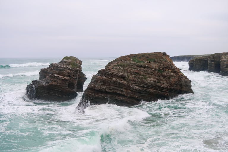 Ocean cliffs with waves crashing against rocks near a rugged coastline.