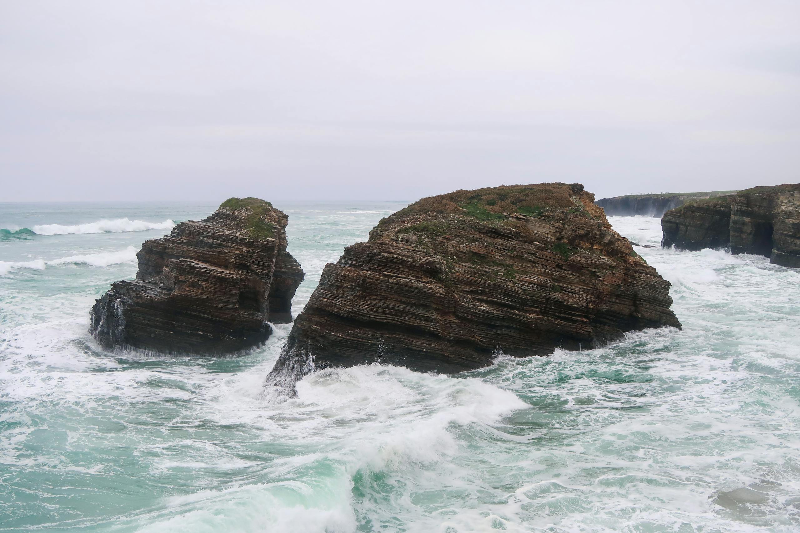 Ocean cliffs with waves crashing against rocks near a rugged coastline.