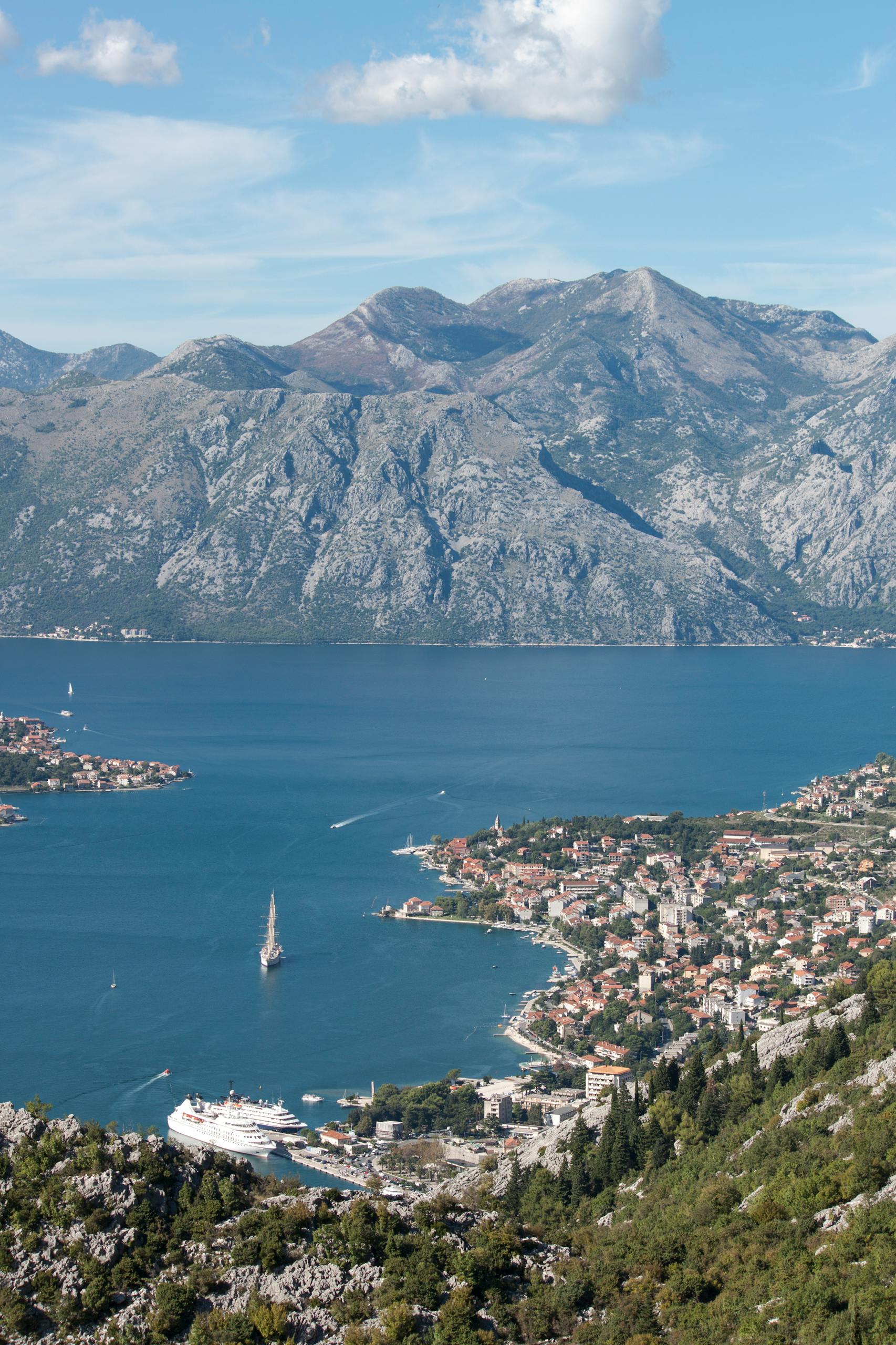 Picturesque view of a coastal town with cruise ships in scenic bay surrounded by towering mountains.