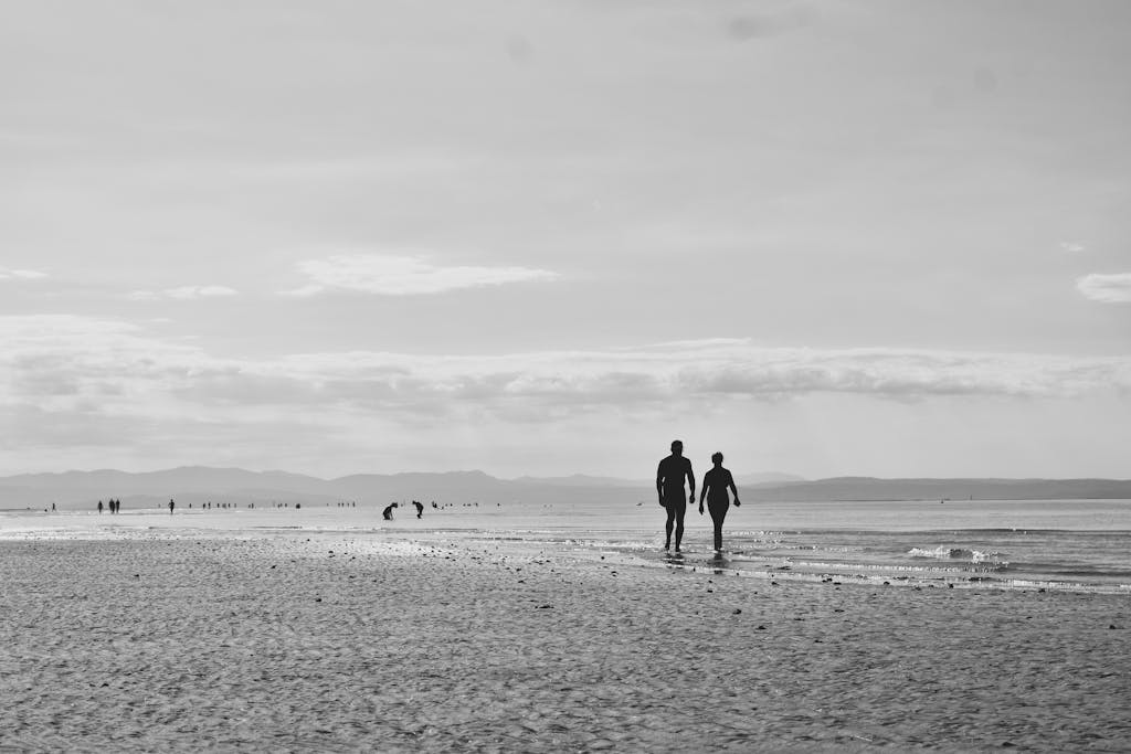 Silhouette of a couple walking on Grado beach in black and white, creating a serene and romantic scene.