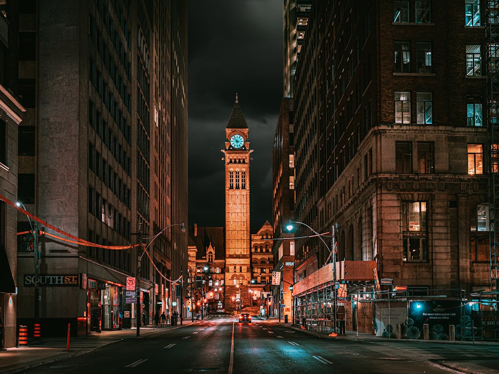 Stunning nighttime view of Toronto's illuminated clock tower framed by city streets and tall buildings.